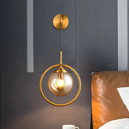 Modern brass circular wall mounted lamp with gold-toned frame and clear glass globe housing an exposed bulb