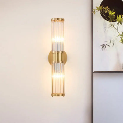 Modern brass clear crystal wall lamp with gold-toned vertical glass rods designed as a sleek bedroom sconce