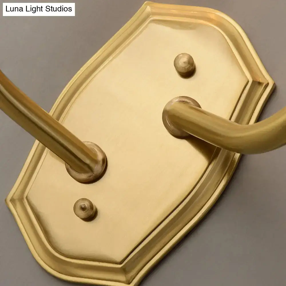 Brass-finished wall-mounted towel rack with ornate shield-shaped backplate and two curved hooks for living room use