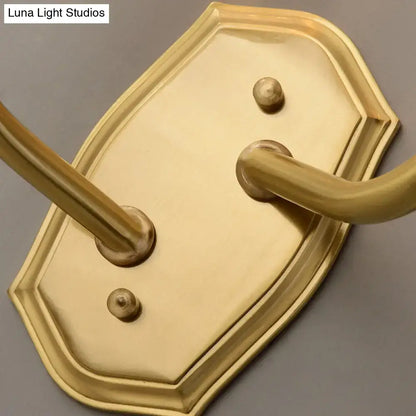 Brass-finished wall-mounted towel rack with ornate shield-shaped backplate and two curved hooks for living room use