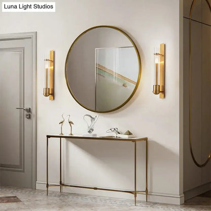 Round gold-framed mirror paired with a modern brass clear glass wall sconce light fixture for bedroom use