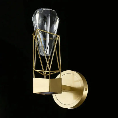 A sleek modern brass crystal rock wall sconce features a gold-toned geometric wireframe cage and crystal pendant