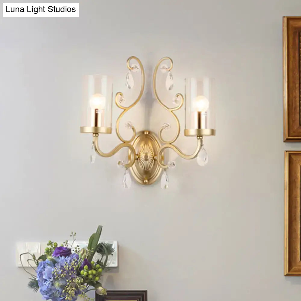 Gold-toned modern brass crystal wall mounted light with two candle-style arms and clear glass shades for bedroom use