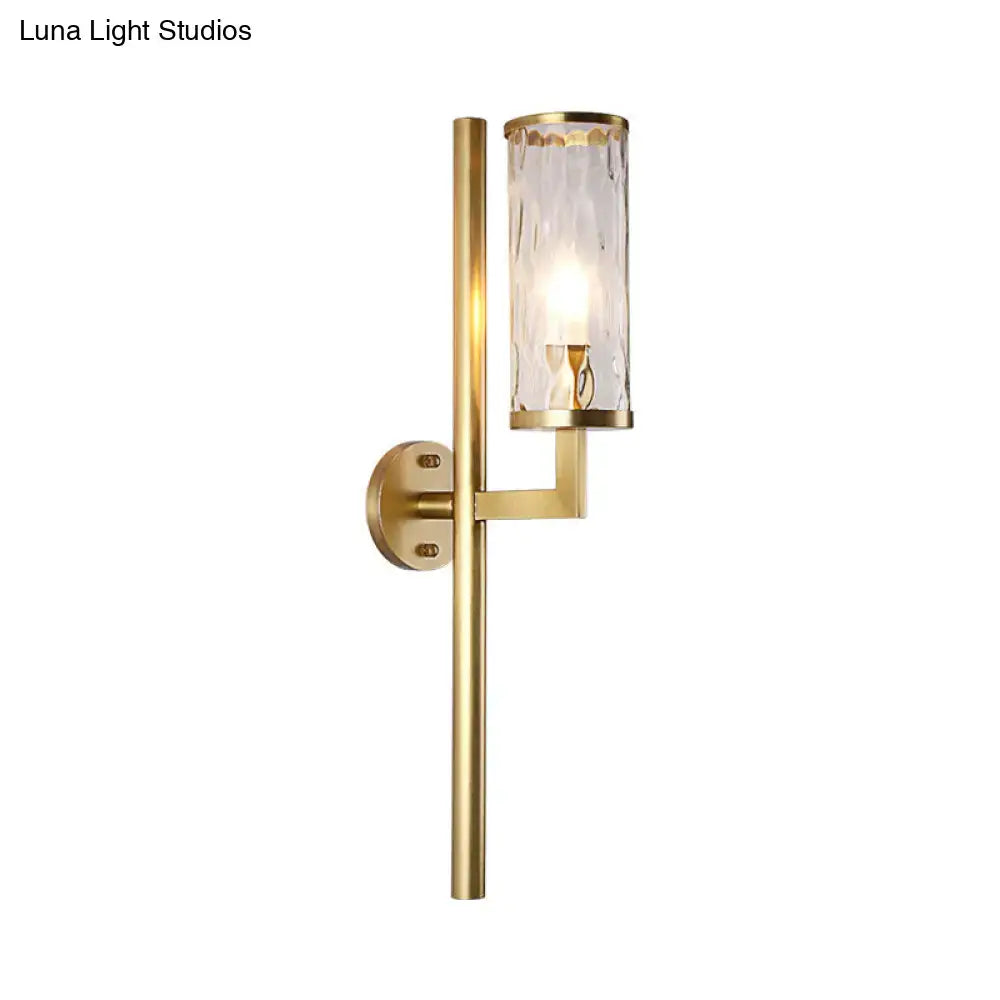 Modern brass cylinder sconce with gold finish and textured clear water glass shade for bedroom wall lighting