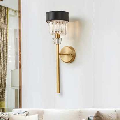 Modern brass cylinder wall sconce with fabric shade in gold tone and dangling crystal accents for bedroom lighting