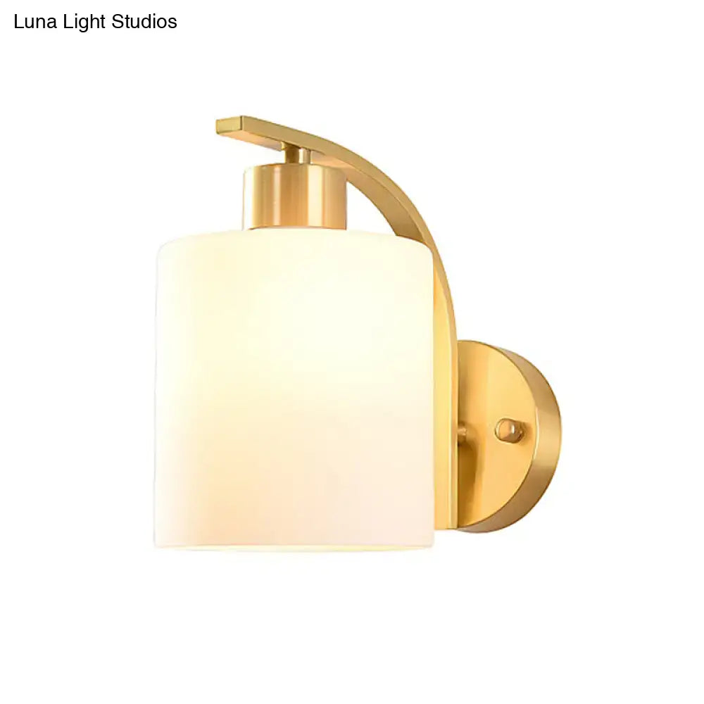 Modern brass cylinder wall sconce with gold finish and frosted milk glass shade for bedroom lighting