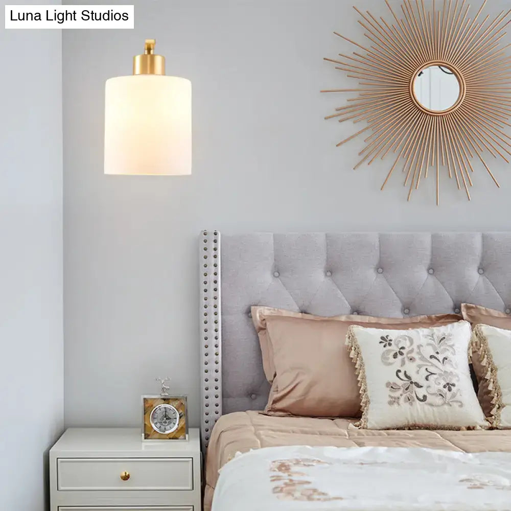 Modern brass cylinder wall sconce with gold finish and milk glass shade for bedroom lighting