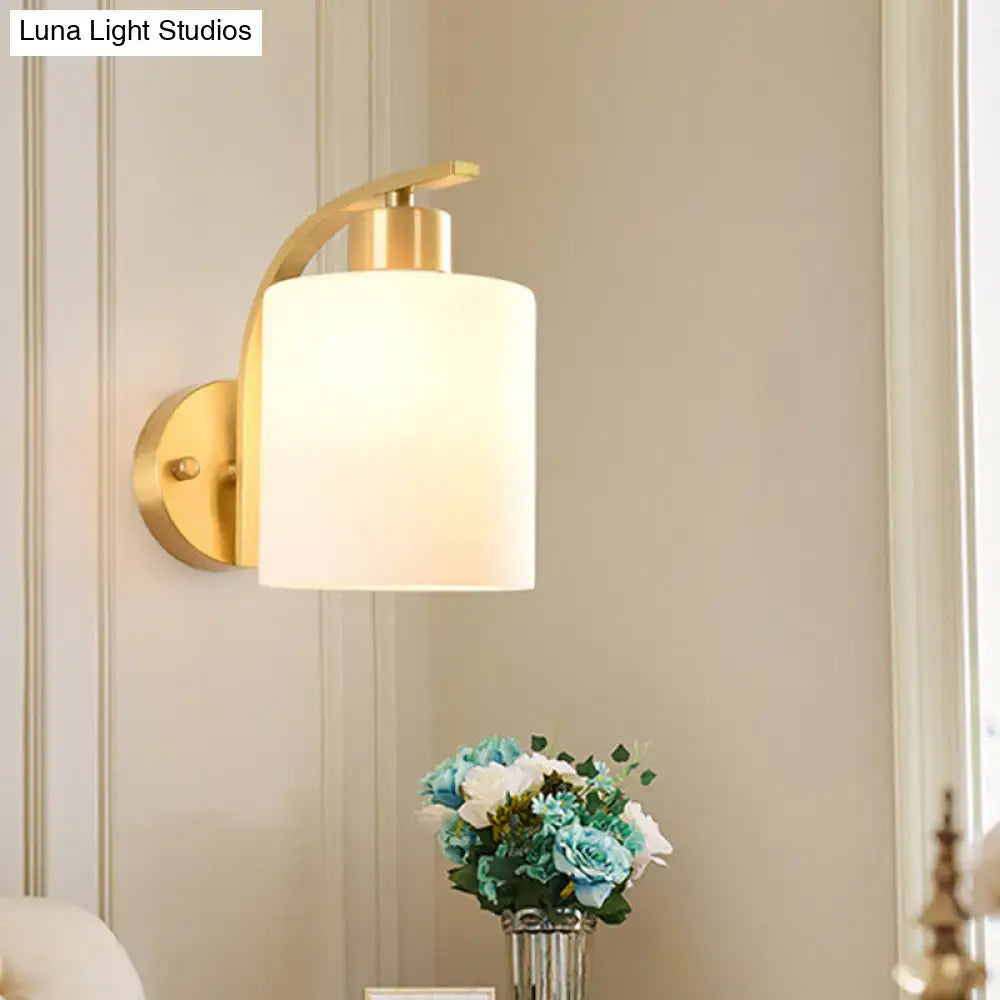 Modern brass cylinder wall sconce with gold finish and a cylindrical milk glass shade for bedroom lighting