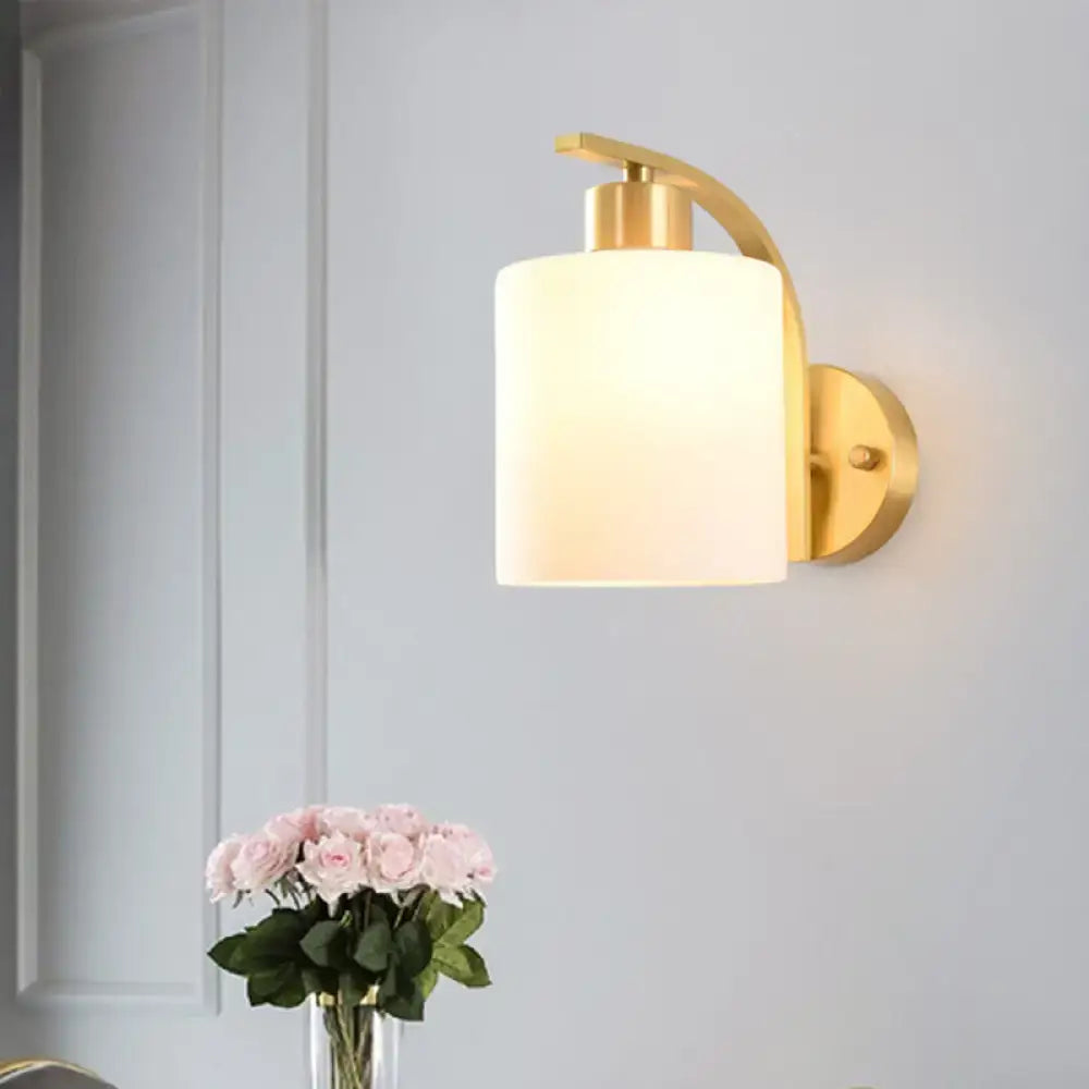 Modern brass cylinder wall sconce with gold tone and frosted milk glass shade for bedroom lighting