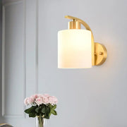 Modern brass cylinder wall sconce with gold tone and frosted milk glass shade for bedroom lighting