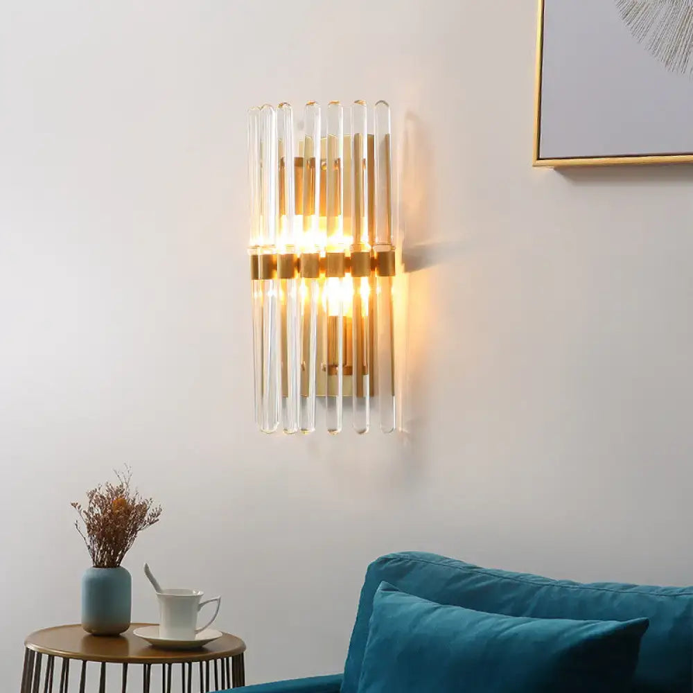 Modern brass finish clear crystal sconce lamp with vertical glass tubes and warm glow for bedroom lighting