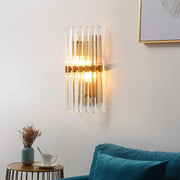 Modern brass finish clear crystal sconce lamp with vertical glass tubes and warm glow for bedroom lighting