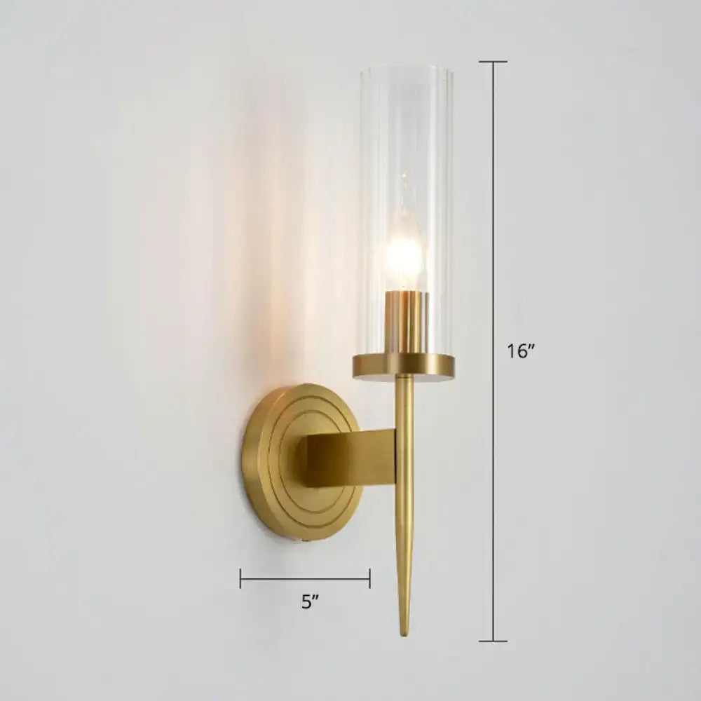 A sleek 16-inch tall brass finish glass tube wall light with a clear cylinder housing an illuminated bulb for living room use