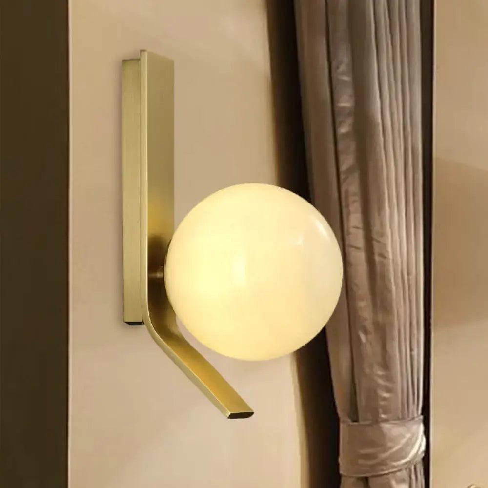 Modern brass wall lamp with a curved metal backplate and smooth spherical frosted glass globe for bedroom use