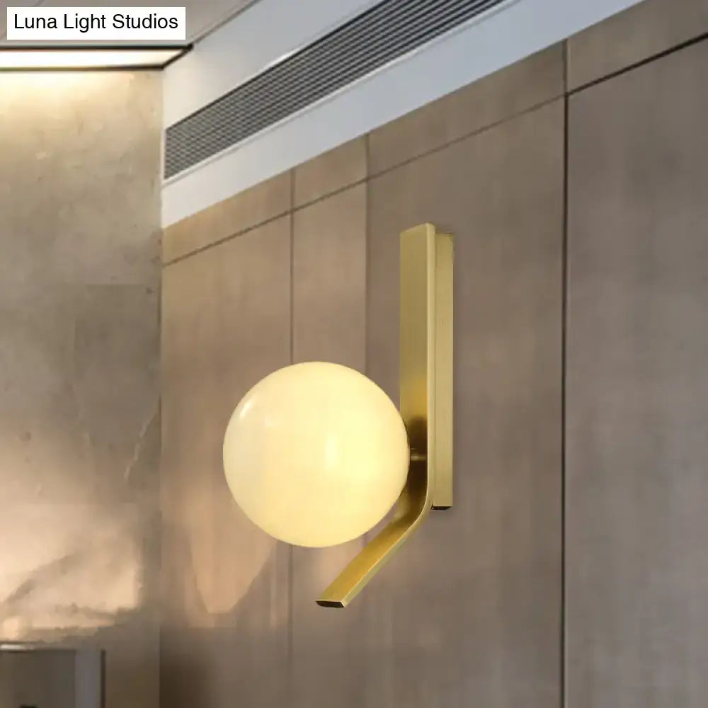 Modern brass wall lamp with frosted glass globe and curved metal backplate for stylish bedroom lighting