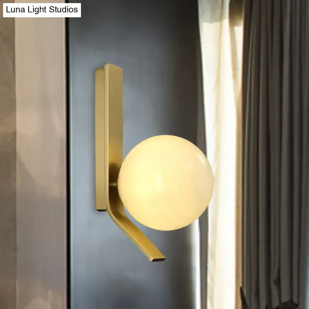Modern brass wall lamp with curved metal backplate and frosted glass globe designed for bedroom lighting