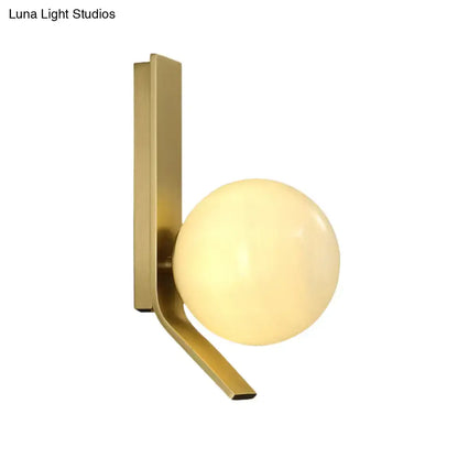 Modern brass wall lamp with curved metal backplate and frosted glass globe for bedroom lighting