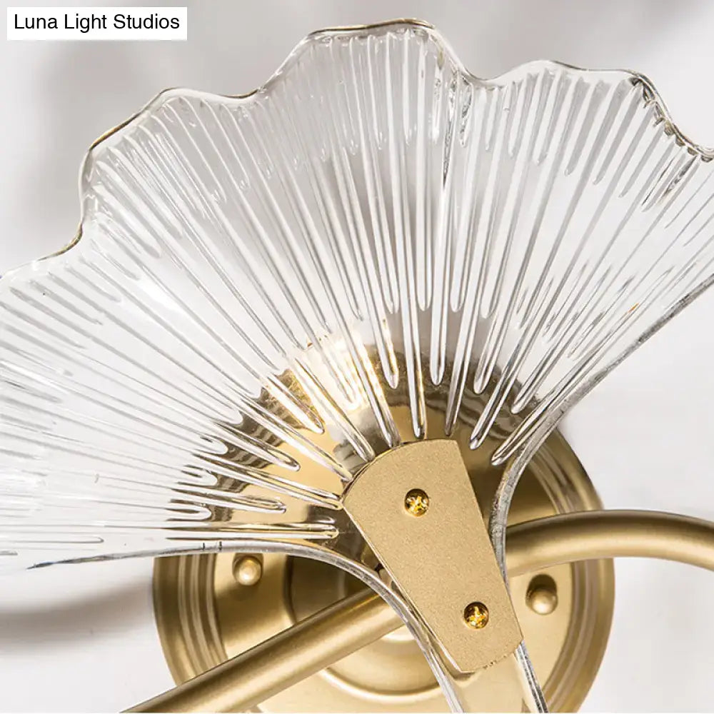 Modern brass ginkgo leaves wall light with clear ribbed glass fan-shaped shade and gold-toned metal frame for bedroom