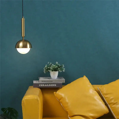 Modern brass glass ball led pendant chandelier with spherical shade hanging above mustard-yellow leather sofa decorbites pendant chandelier