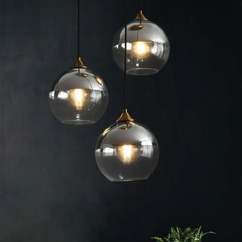 Three modern brass glass ball pendant lights with brass accents hang against a dark background for dining decorbites pendant light