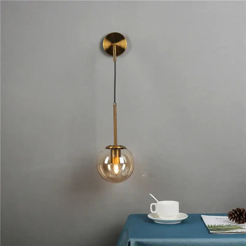 A modern brass wall lamp with a spherical amber glass ball and exposed bulb for bedroom decorbites glass ball lighting