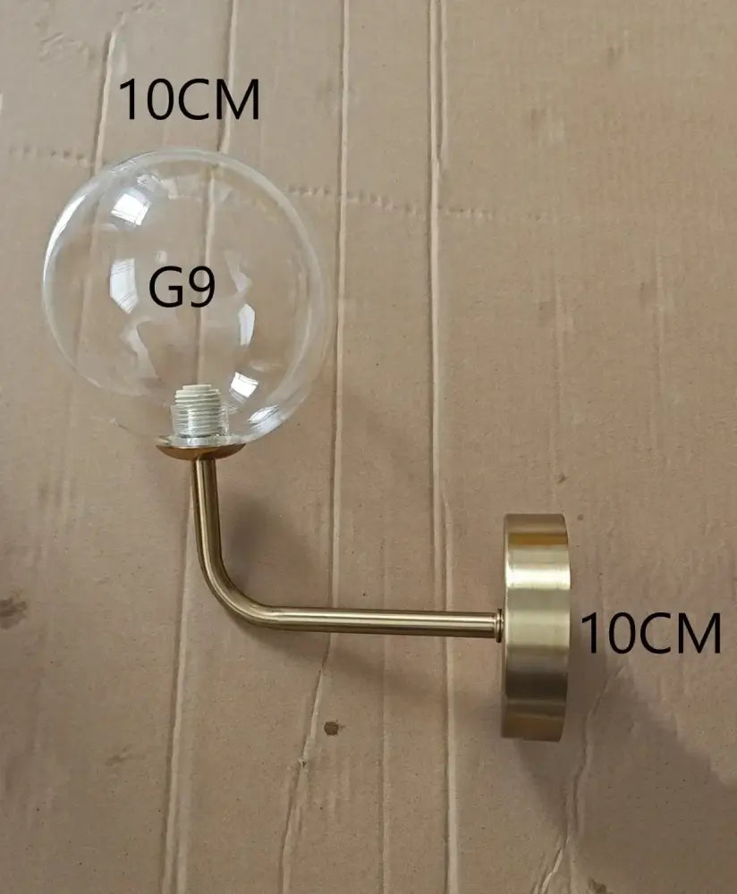 Modern brass glass ball wall lamp featuring a clear glass globe with brass-finished metal arm for stylish bedroom decorbites lighting
