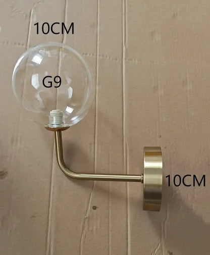 Modern brass glass ball wall lamp featuring a clear glass globe with brass-finished metal arm for stylish bedroom decorbites lighting