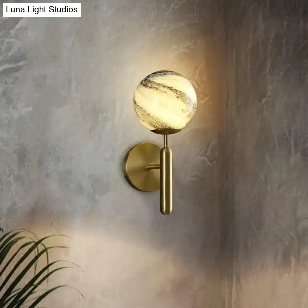 Modern brass glass globe wall mount light with marbled spherical globe emitting warm light for living room sconce