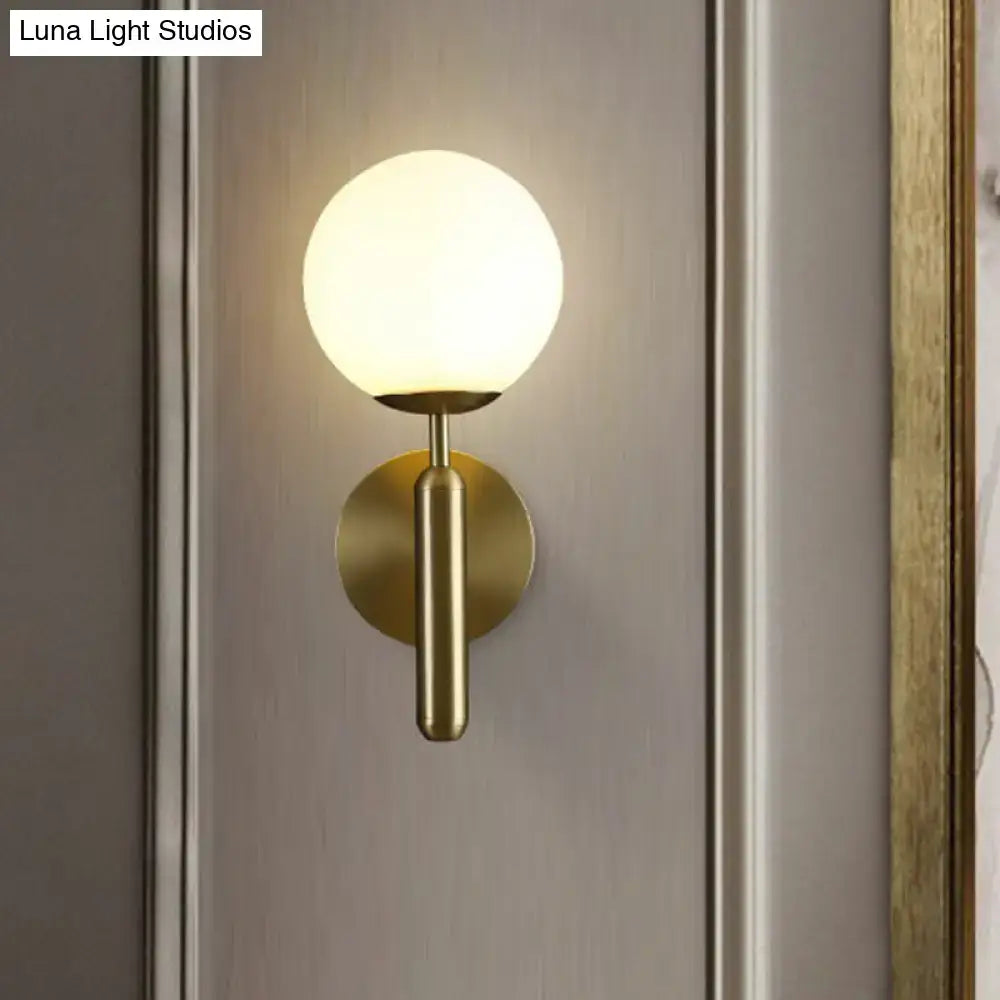 A modern brass wall mount light with a frosted glass globe shade ideal for living room sconces