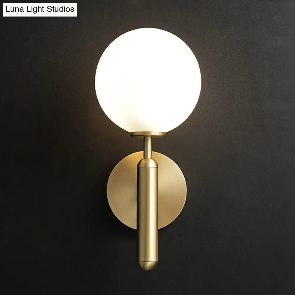 A sleek brass wall mount light with frosted glass globe and cylindrical stem for modern living room decor