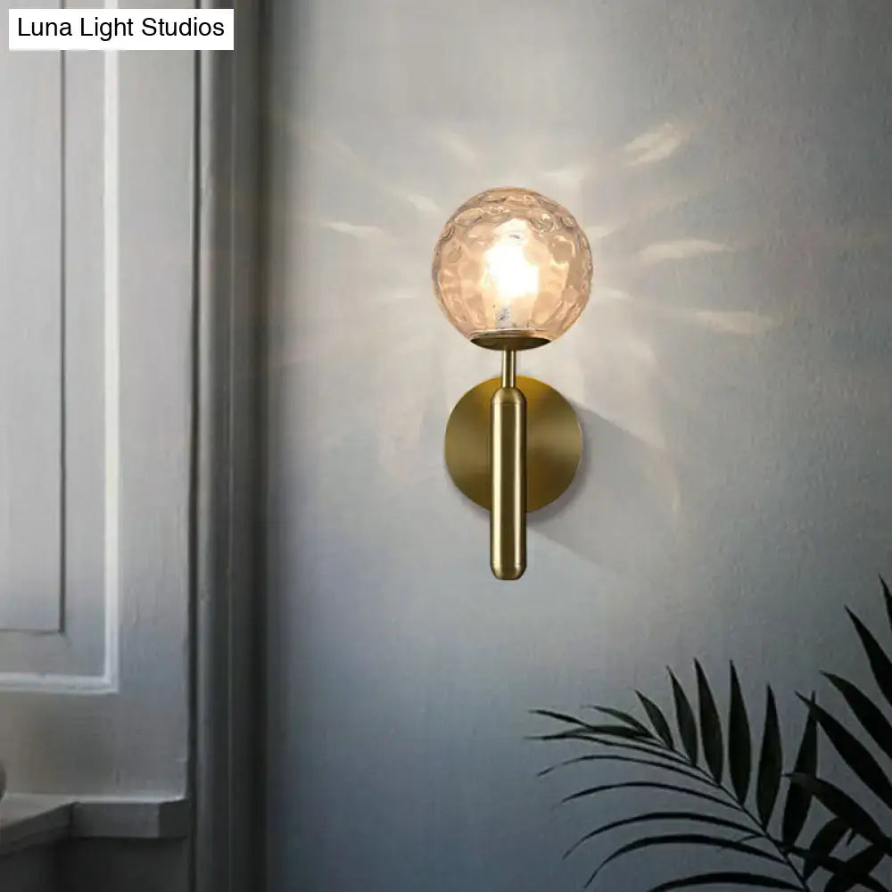 A warm-toned textured glass globe wall mount light with brass finish metal base and stem for living room decor