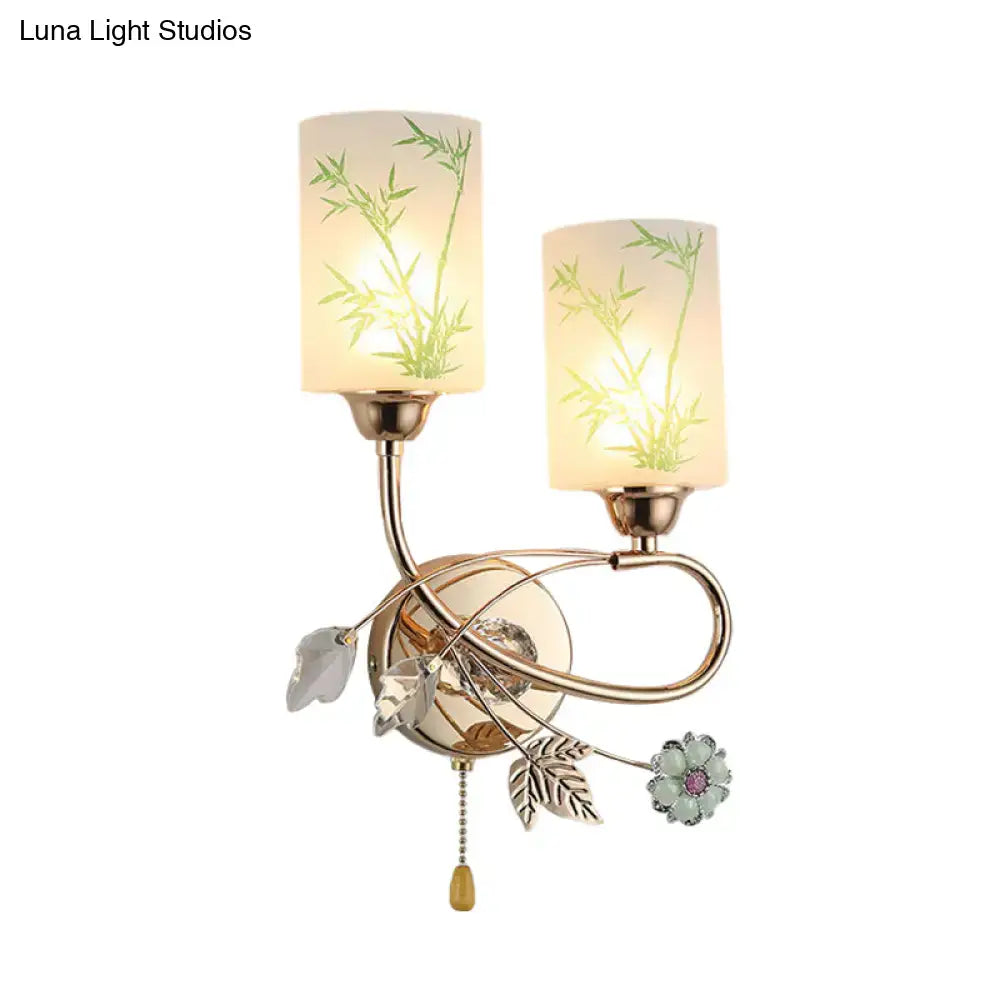 Modern brass wall lamp with pull chain featuring two frosted glass shades with green bamboo etchings