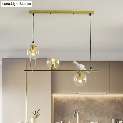 Modern brass global island lamp with gold-toned pendant, three glass globe bulbs, and white ceramic bird detail