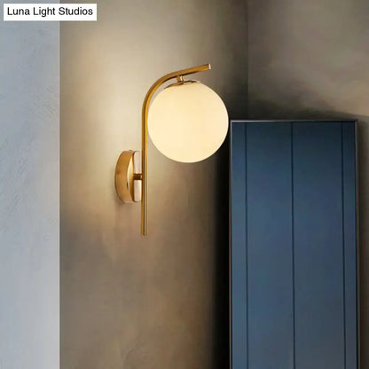 Gold-toned modern brass bedside lamp with curved arm and frosted glass globe inch fixture for bedroom lighting