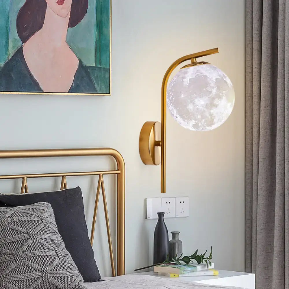 A sleek gold-toned modern brass bedside lamp with a translucent moon-shaped frosted glass globe inch fixture