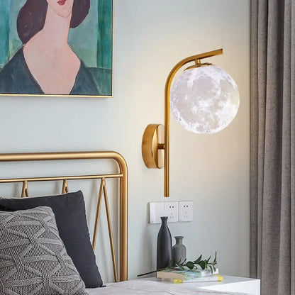 A sleek gold-toned modern brass bedside lamp with a translucent moon-shaped frosted glass globe inch fixture