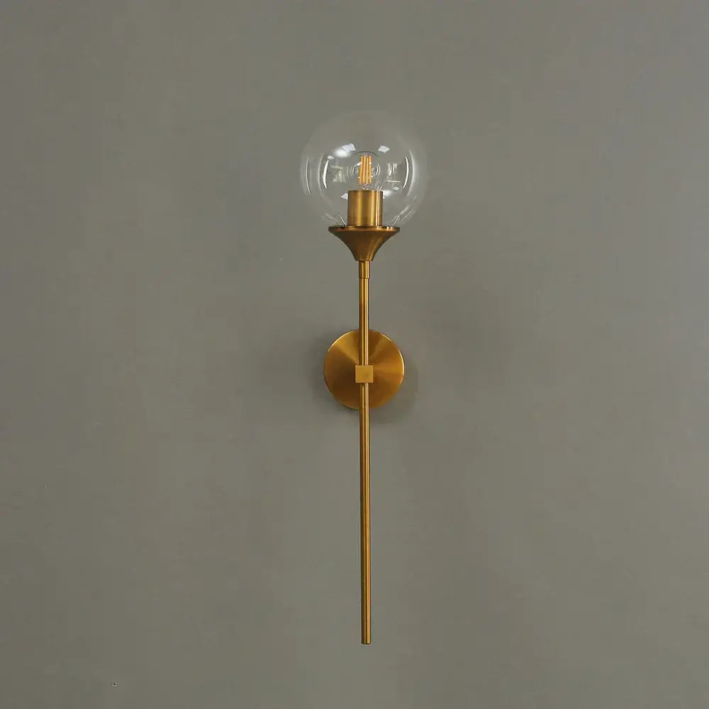 A sleek modern brass golden glass ball wall lamp with a slender stem and exposed filament bulb for bedroom decorbites
