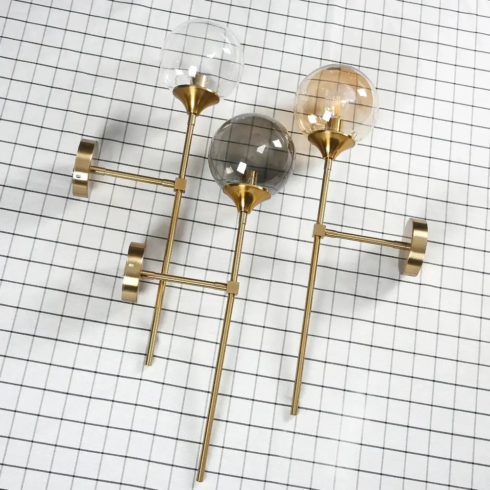 Modern brass golden glass wall sconce with three spherical shades in clear smoky gray and amber tones for bedroom decor