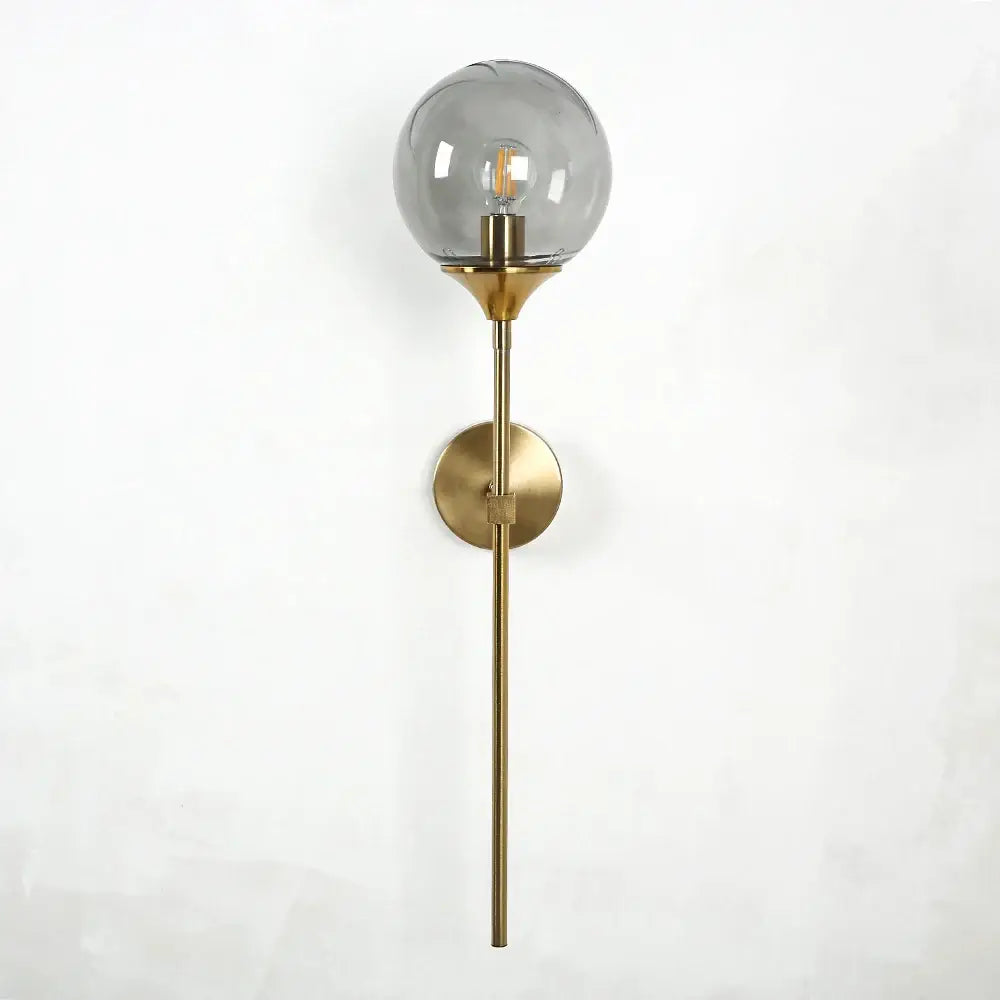 A sleek modern brass wall sconce with a smoked golden glass globe and exposed filament bulb decorbites golden glass wall