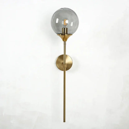 A sleek modern brass wall sconce with a smoked golden glass globe and exposed filament bulb decorbites golden glass wall