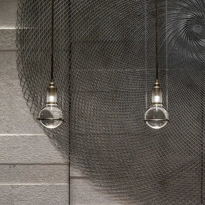 Two clear glass globe pendant lights with brass fixtures hang against a dark wire mesh backdrop decorbites crystal ball led