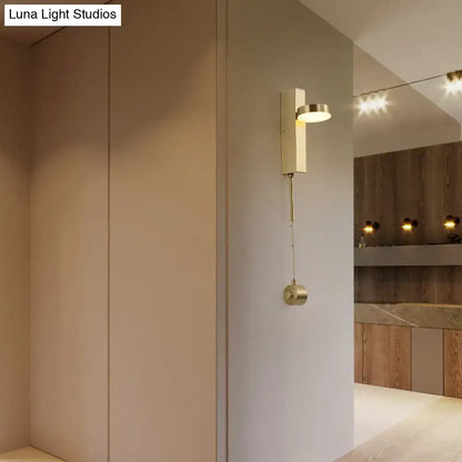 Modern brass l-shaped wall sconce with pull chain featuring a rectangular body and circular light fixture for living room