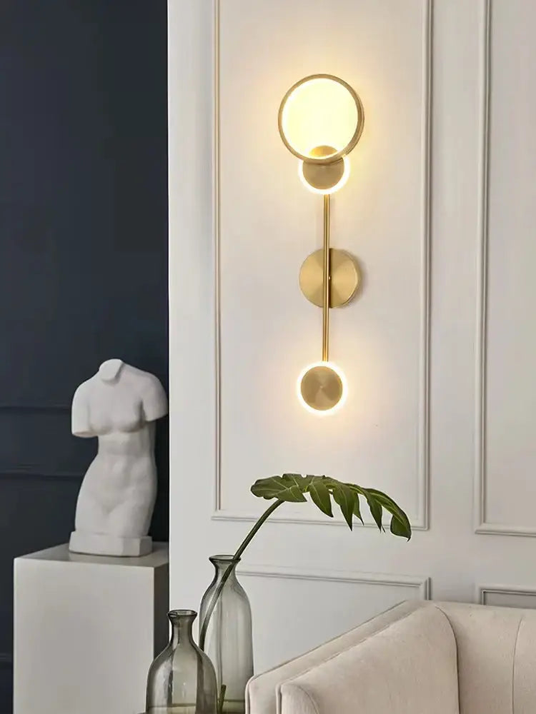 Modern brass led wall light with three gold-toned circular discs stacked vertically on a slender rod for living room decorbites brass led
