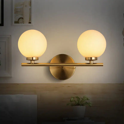 Modern brass bedroom sconce light fixture with gold-toned finish and two frosted glass product shade bulbs