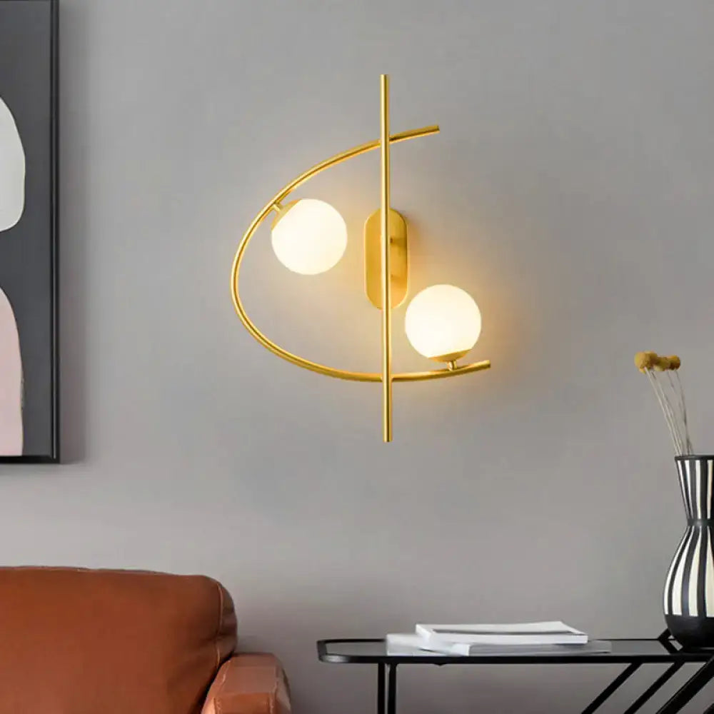 Modern brass wall sconce with gold-toned curved frame and two frosted milk glass ball shades for living room lighting