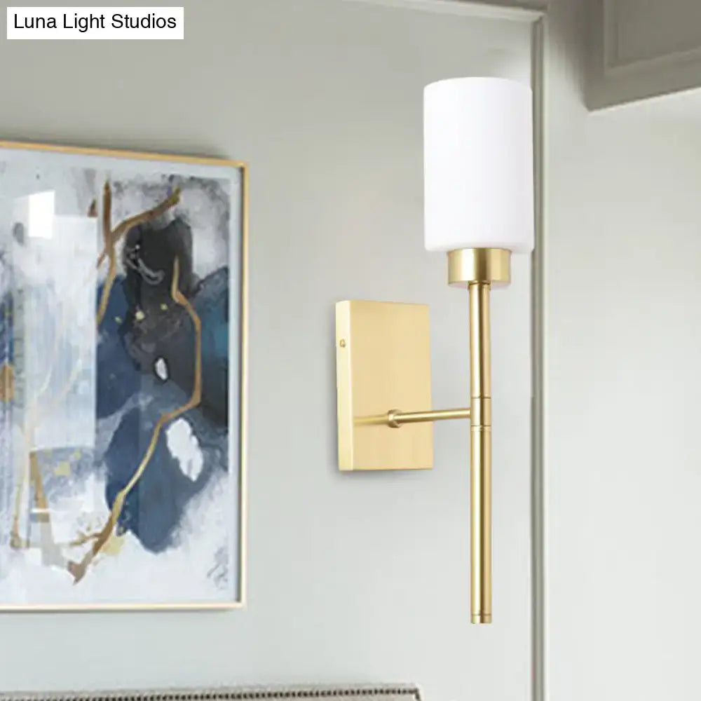 Modern brass wall light with gold-toned fixture and cylindrical white opal glass tube shade for bedroom sconce lighting