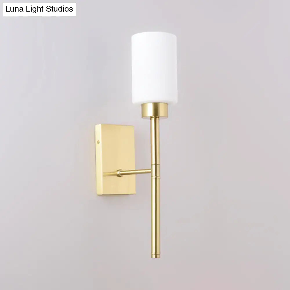 Modern brass opal glass tube wall light featuring a gold-toned sconce with a cylindrical white opal glass shade for bedroom use