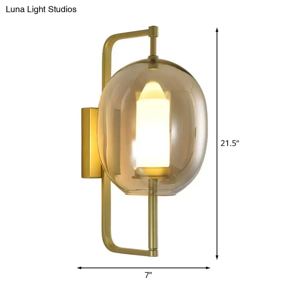 Modern brass wall sconce with oval clear glass shade and smoked glass globe housing illuminated candle bulb