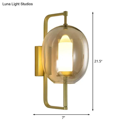 Modern brass wall sconce with oval clear glass shade and smoked glass globe housing illuminated candle bulb