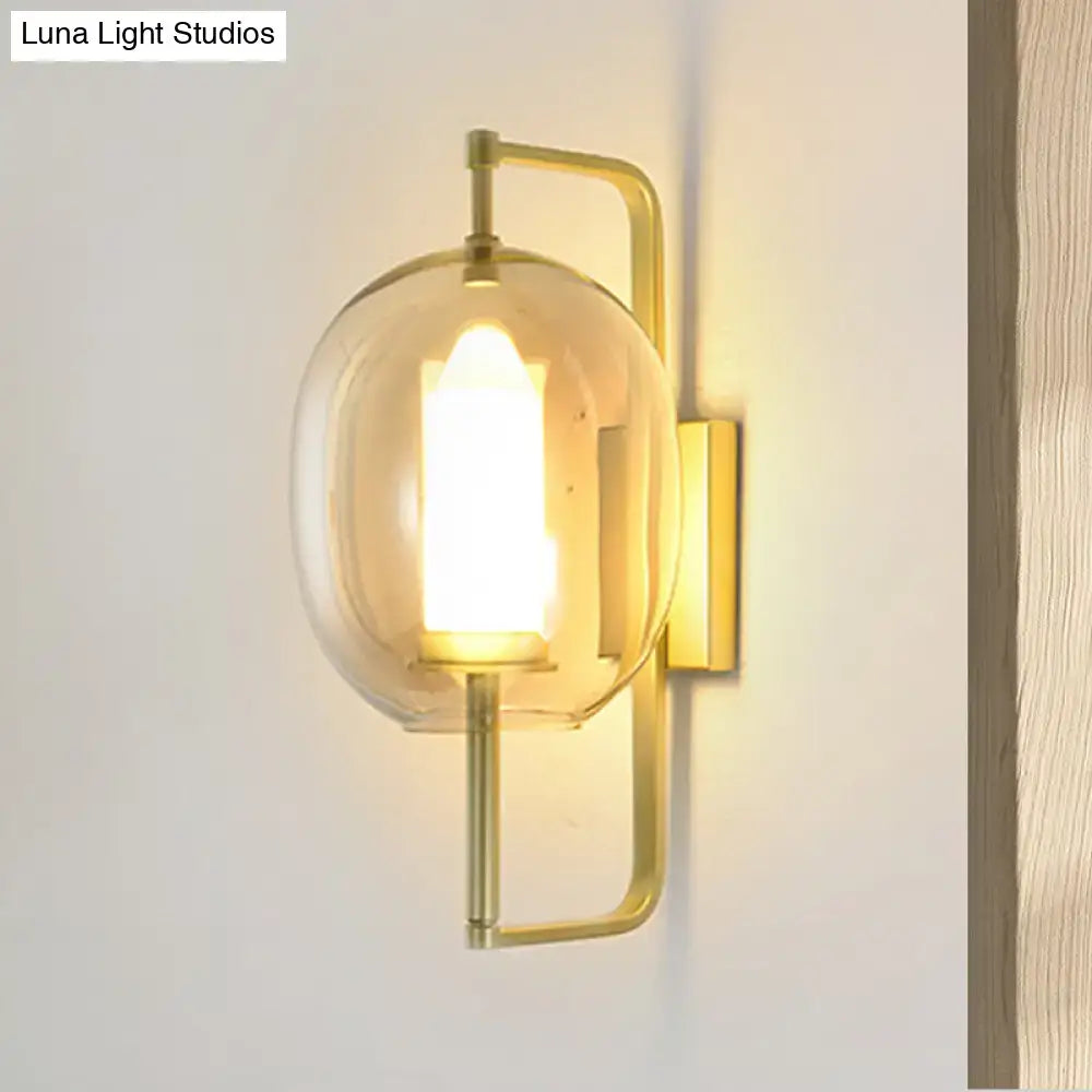 Modern brass wall sconce with gold-toned finish and oval clear glass shade housing an illuminated led bulb
